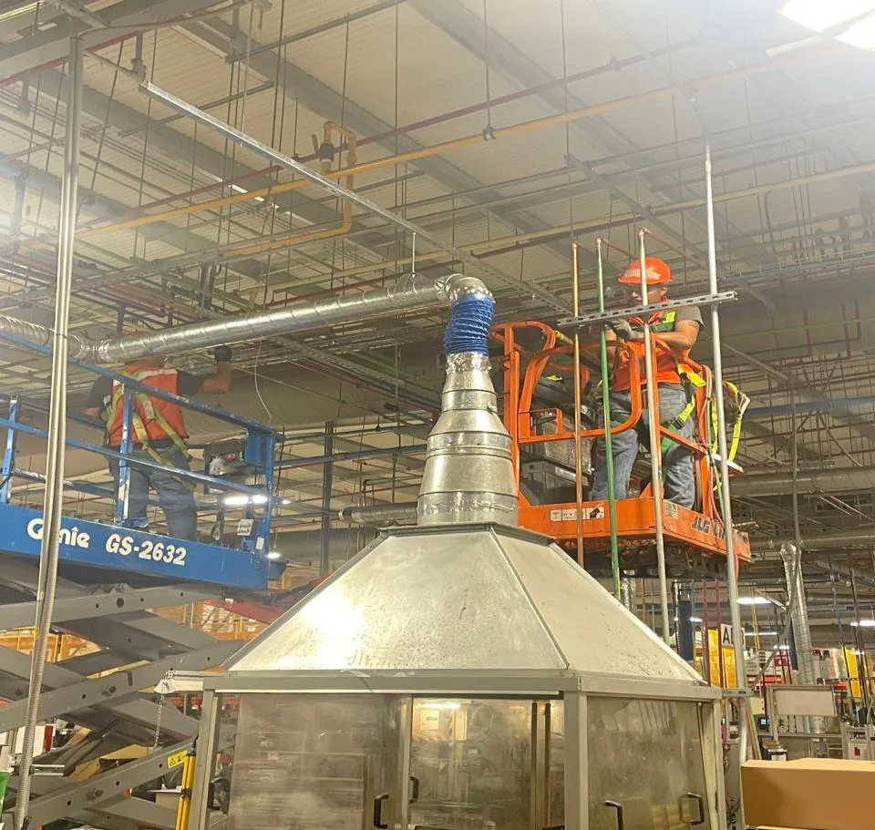 Campana de extracción piramidal de acero inoxidable conectada a espiroducto con manguera flexible azul, con técnicos en plataformas de tijera